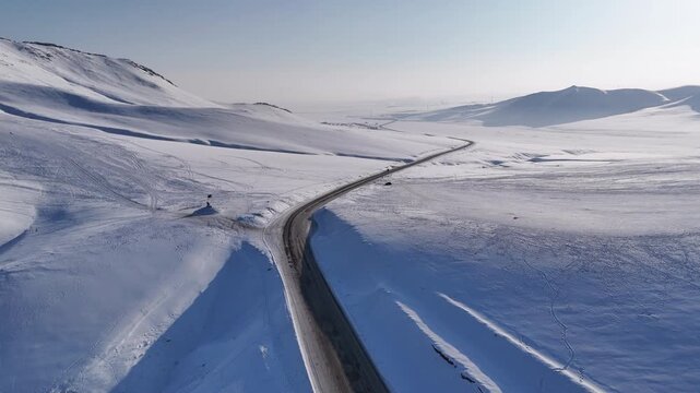 Aerial View of a Winding Road Through Vast Snowy Hills in Winter Mongolia (겨울 몽골의 광활한 눈 덮인 언덕을 가로지르는 구불구불한 도로의 드론 항공 뷰)