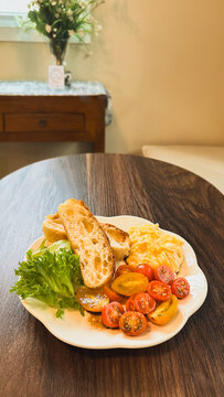 Healthy breakfast with scrambled eggs, toasted, sliced cherry tomato, and fresh greens on wooden surface.