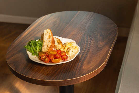 Healthy breakfast with scrambled eggs, toasted, sliced cherry tomato, and fresh greens on wooden surface.