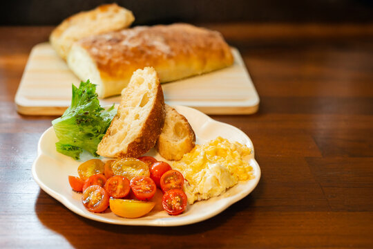 Breakfast plate with creamy scrambled eggs, sliced cherry tomato salad, crusty ciabatta slices.