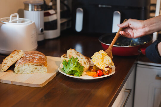 Woman chef serving scrambled eggs with cherry tomatoes, fresh lettuce, and artisan bread in cafe.