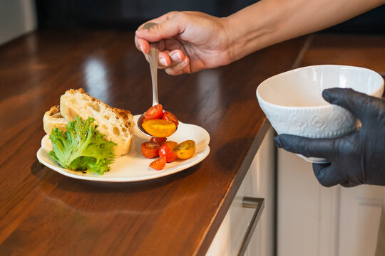 Woman chef serving fresh cherry tomato salad with toasted baguette slices on a white plate.