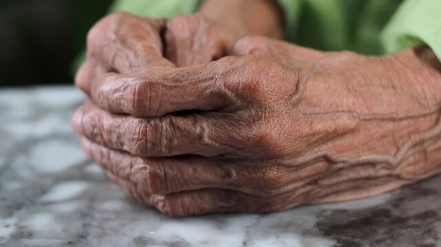 Elderly hands resting on a marble table in a simple setting