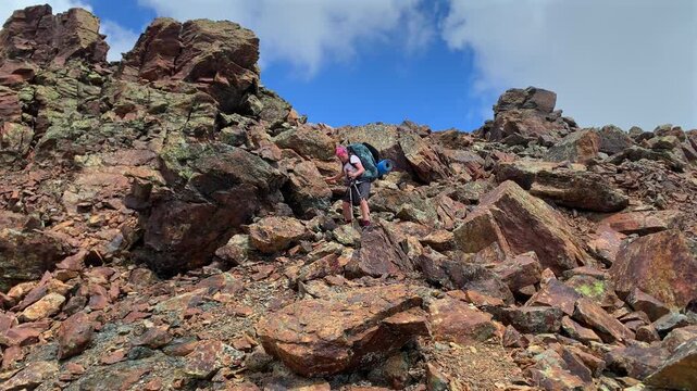 Female hiker descending rocky slope in wide shot on a mountain trail, showing trekking, route navigation and outdoor adventure travel in rugged alpine terrain for tourism and expedition footage