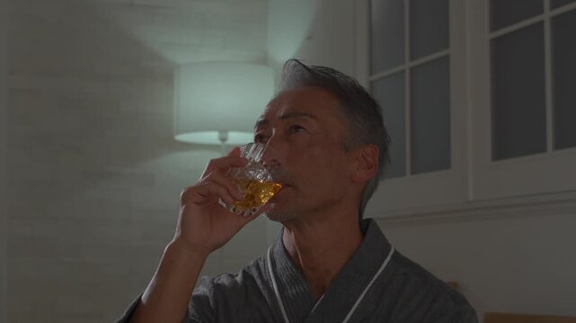 寝室でウイスキーを飲むシニア男性