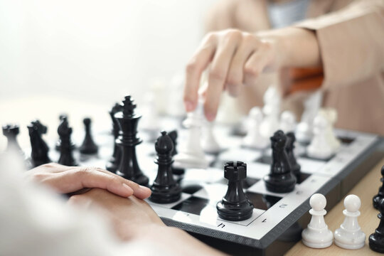 Hand moving white piece on chessboard during strategic game for corporate business planning, leadership competition, decision management concept