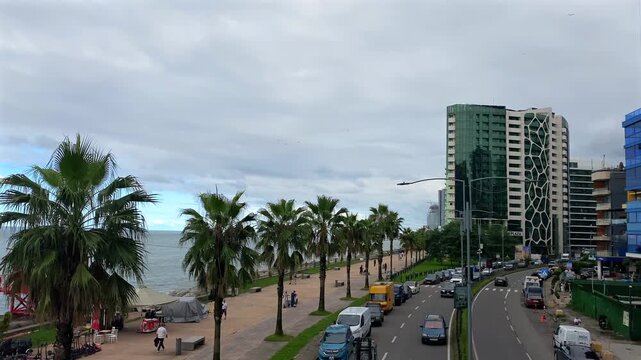 Traffic moving along Batumi seaside boulevard, elevated view, beside palm-lined promenade and Black Sea coast with high-rise buildings, urban tourism, transport