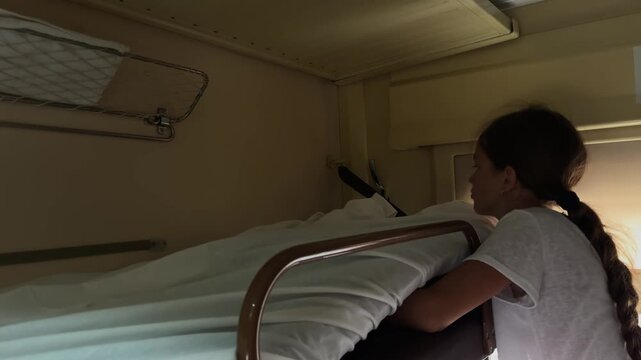 The girl covers her resting place on the train with white bed linen during the journey in her compartment or open sleeper car.