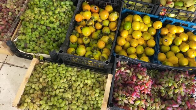 Grapes and persimmons are displayed for sale in crates, viewed from above at a produce stall. Assorted fresh fruit illustrates grocery retail, market merchandising and everyday shopping