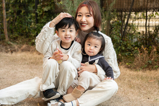 A joyful mother embracing her two children while sitting on the grass outdoors.