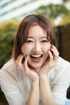 Close-up portrait of a smiling woman holding her face with both hands outdoors.
