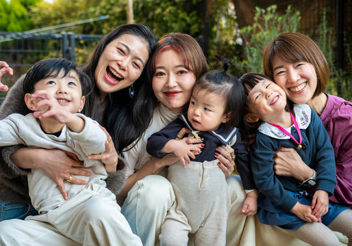 Group portrait of mothers and children laughing joyfully together outdoors.