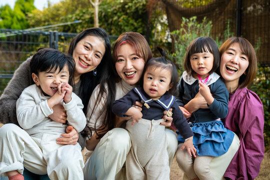 Warm group portrait of mothers and children smiling together in a sunny yard.