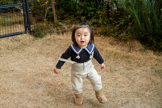 A cute toddler walking happily on a grassy lawn outdoors.