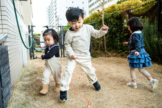A young boy jumping rope outdoors with a toddler and girl in the background.