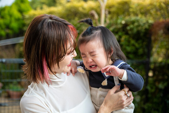A mother holding and consoling her crying toddler in an outdoor yard.