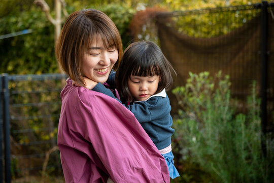 A smiling mother holding her young daughter securely in a sunny outdoor setting.