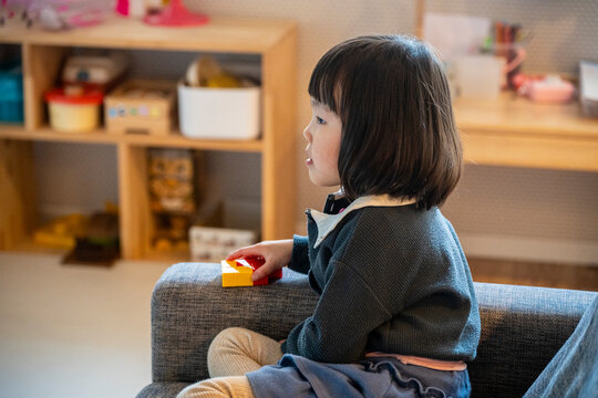 A little girl sitting on a cozy sofa playing with building blocks indoors.