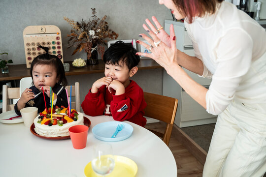 A woman cheerfully clapping hands while children enjoy a birthday cake celebration.