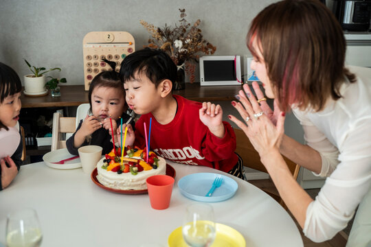 A joyful birthday scene with a boy blowing candles and an adult clapping in delight.