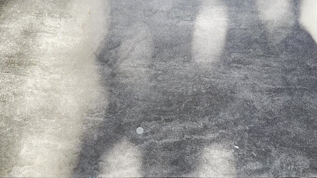 Soft abstract tree shadows fall across a speckled grey textured floor, creating a calm minimal visual with diffused sunlight, organic forms, and tactile surface detail.