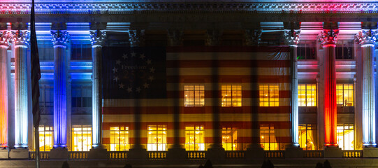 Obraz premium American flag across government building. American freedom banner on facade. Illuminated columns frame American celebration. July fourth honors American independence.