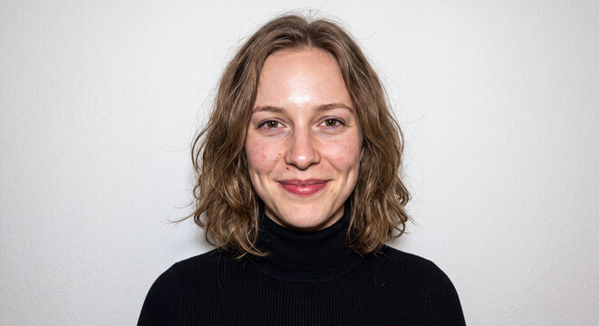Warm studio headshot of a smiling woman with wavy blonde hair wearing a black top against a plain grey background. Ideal for corporate, business and lifestyle profile use.