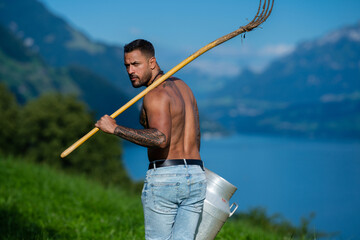 Obraz premium Eco farm portrait with muscular dairy farmer. Traditional eco farm lifestyle with rustic pitchfork. Eco farm worker carrying milk can outdoors. Shirtless man in eco farm dairy portrait.