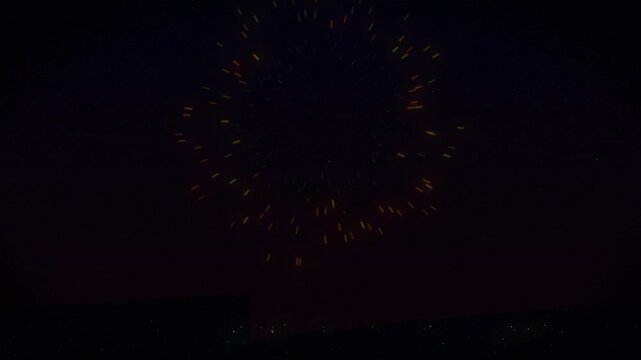 Bright golden firework exploding into glowing sparks against dark night sky with city silhouette in background