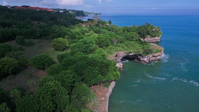 Coastal arches and limestone formations. Waves surge through caves beside rugged cliffs. Green cliffs overlook sheltered inlets with textured shoreline patterns,Bali