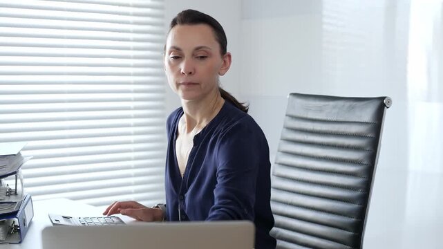 Professional female working at desk, calculating finances, writing notes, managing business documents in contemporary workspace. Audit and taxes in business