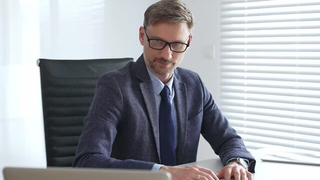 Adult businessman wearing blue suit and tail is concentrating while writing on a document at his desk in a bright, modern office, demonstrating professionalism and efficiency. Business people concept