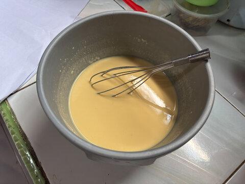Liquid yellow cake batter mixed with a wire whisk in a grey plastic bowl on a kitchen counter