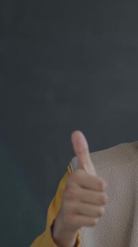 Slow motion portrait of satisfied African American man showing thumbs-up hand gesture smiling looking at camera on black studio background