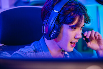 Close up of cheerful Asian man gamer talking into headset microphone while playing online game © SpaceOak