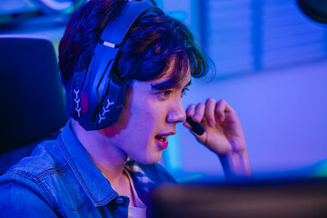 Close up of cheerful Asian man gamer talking into headset microphone while playing online game © SpaceOak