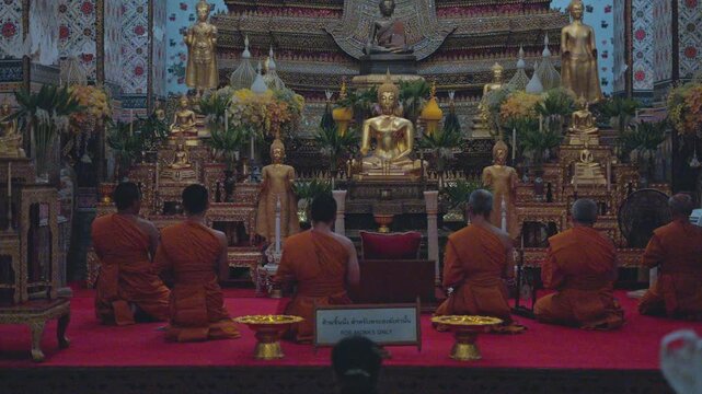 Buddhist monks in orange robes praying inside the wat arun temple in bangkok, thailand