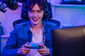 Happy Asian man gamer in headset holding gamepad and playing video game in neon gaming room © SpaceOak