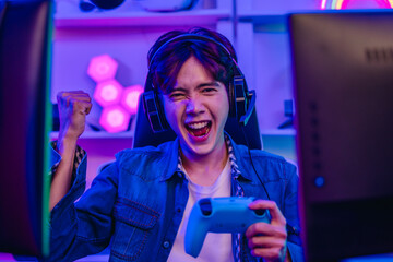 Happy Asian man gamer in headset holding gamepad and playing video game in neon gaming room © SpaceOak