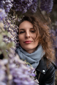 Spring botanical portrait of a young adult woman surrounded by purple wisteria blossoms in a serene garden