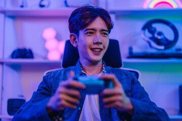 Focused Asian man gamer holding gamepad and playing video game in neon lit gaming room © SpaceOak
