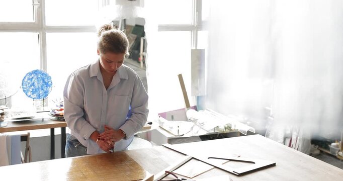 Young woman artisan working on custom glass project on worktable in craft studio cutting material with hand cutter during production process preparing workpieces for handmade decor details. Copy space