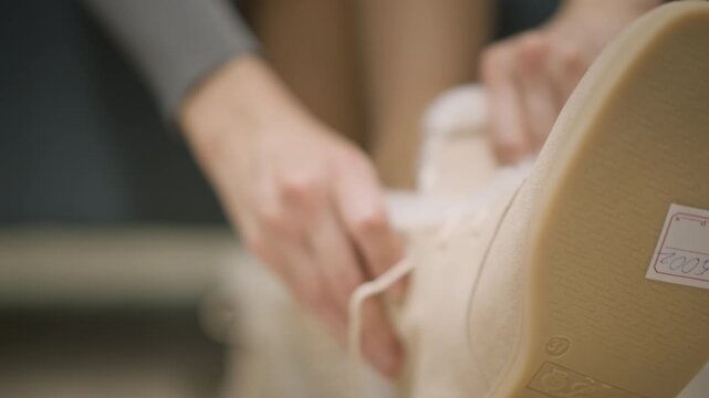 Close up of hands adjusting beige suede shoe with white fur lining focusing on texture and details. person manipulates laces while seated in indoor setting during daylight emphasizing