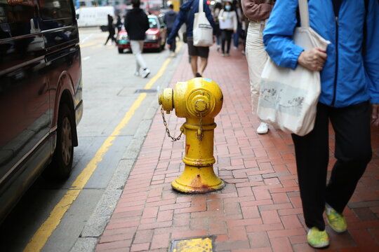 Bright yellow fire hydrant in a busy city sidewalk scene with pedestrians and a black van. Suitable for urban backgrounds.