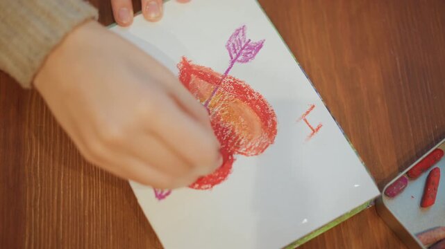Close up of hand coloring arrow through heart on paper with crayons showing detailed texture and vibrant colors. scene features soft lighting over wooden table background where art supplies