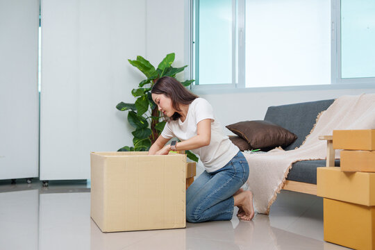 Asian woman packing goods into large cardboard box at home for e-commerce delivery