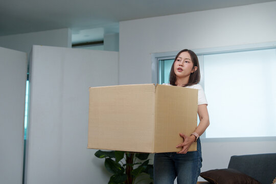 Asian woman lifting heavy cardboard box for home moving or delivery