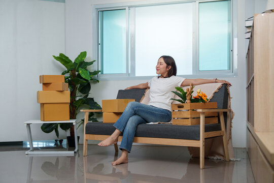 Asian woman relaxing on sofa among cardboard boxes after moving into home