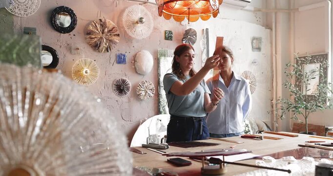 Female craft business partners reviewing prepared glass elements for custom project developing product concept discussing design and visual harmony sorting materials experimenting with color decisions