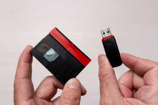 A close-up shot of a man holding a MiniDV video cassette and a modern USB flash drive side by side.